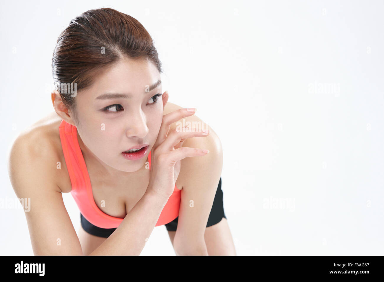 Woman in sportswear bending her upper body down and looking aside with her hand placed on her cheek Stock Photo