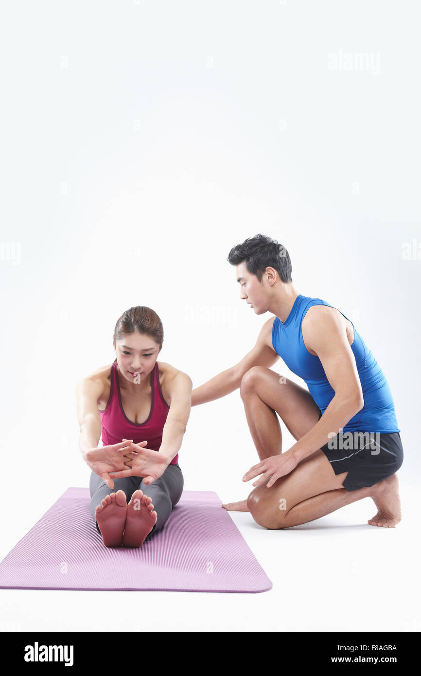 Woman on yoga mat stretching her upper body forward and man coaching her Stock Photo