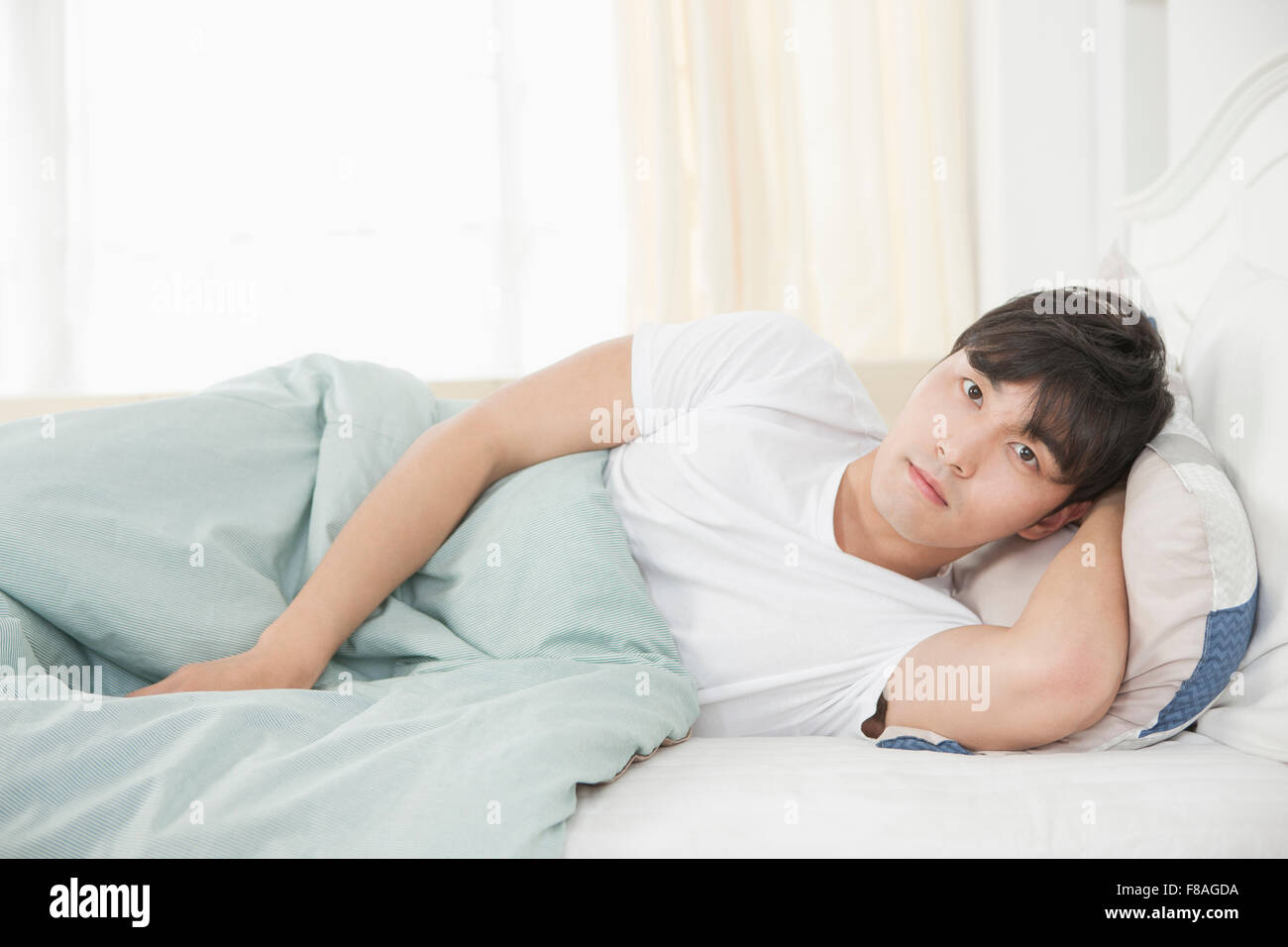 Man staring forward lying on his side with one hand under his head Stock Photo