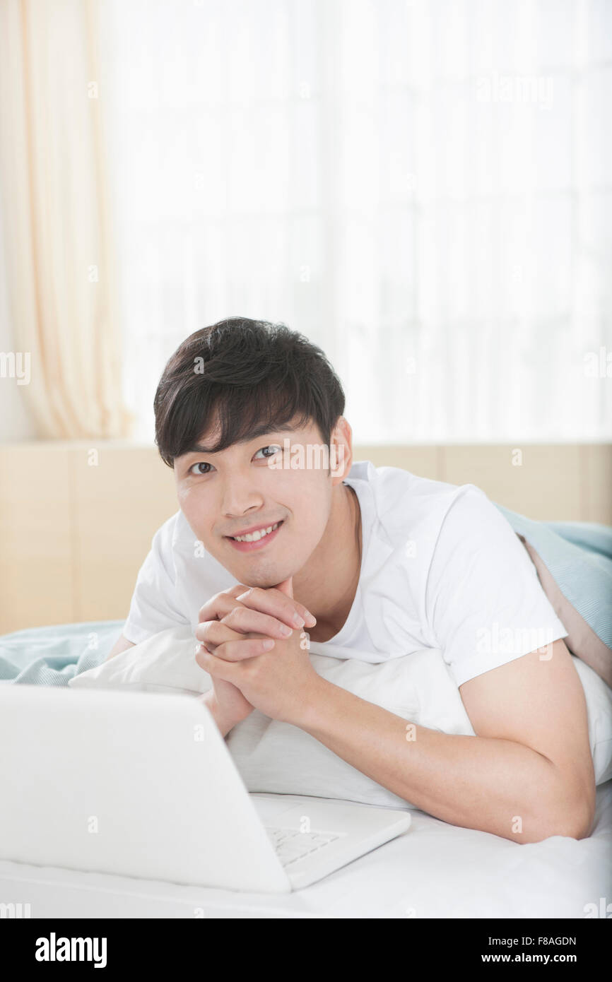 Man lying on his stomach on bed with computer and folding his hands Stock Photo