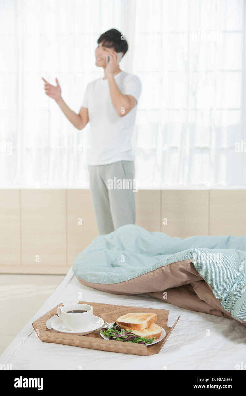 Breakfast tray on bed with the background of a man talking on the phone with hand gesture Stock Photo