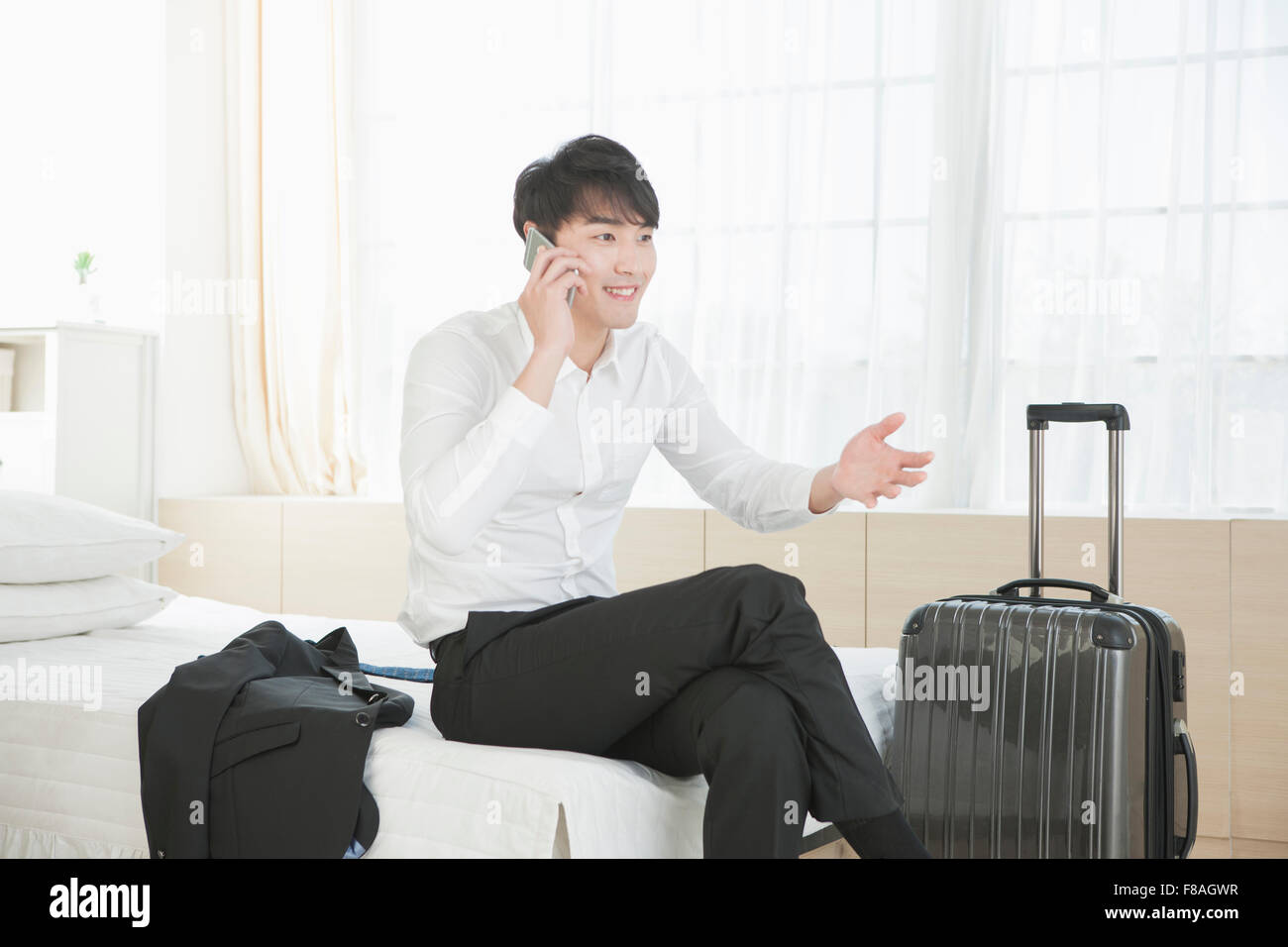 Businessman talking on the phone with hand gestures and legs crossed on bed Stock Photo