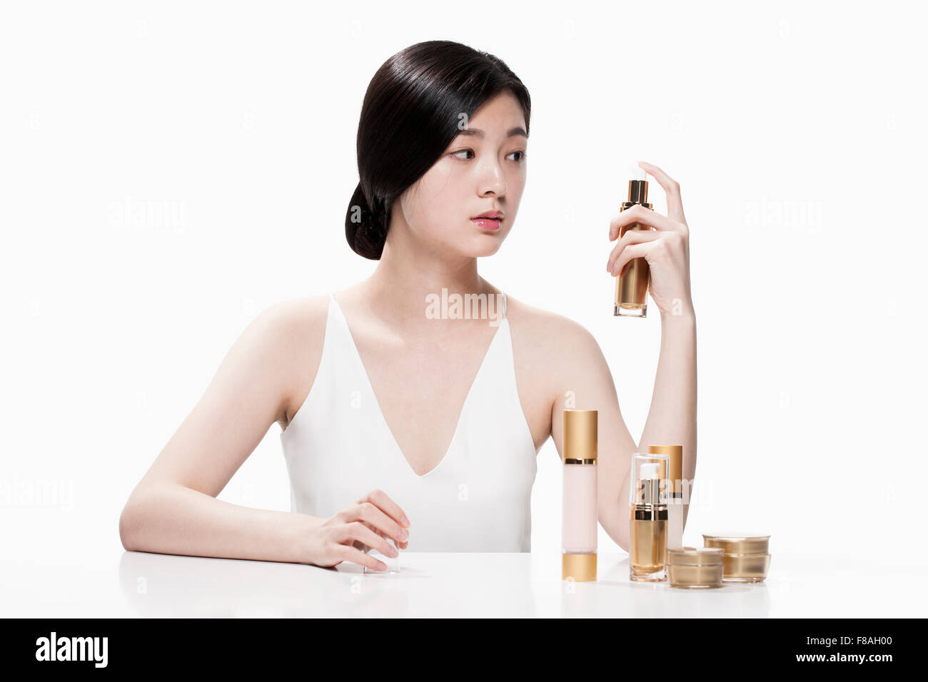 Woman seated at the table holding a skincare product with one hand and staring at the product Stock Photo