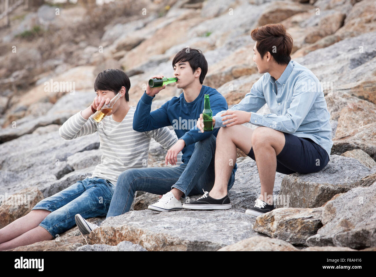Three young men sitting on rocks and drinking beer Stock Photo