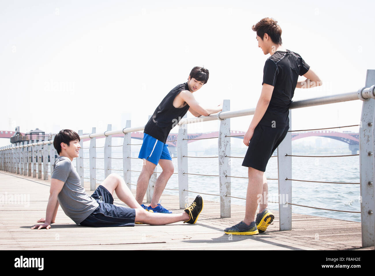 Three men in sportswear relaxing at the fence placed along the river Stock Photo