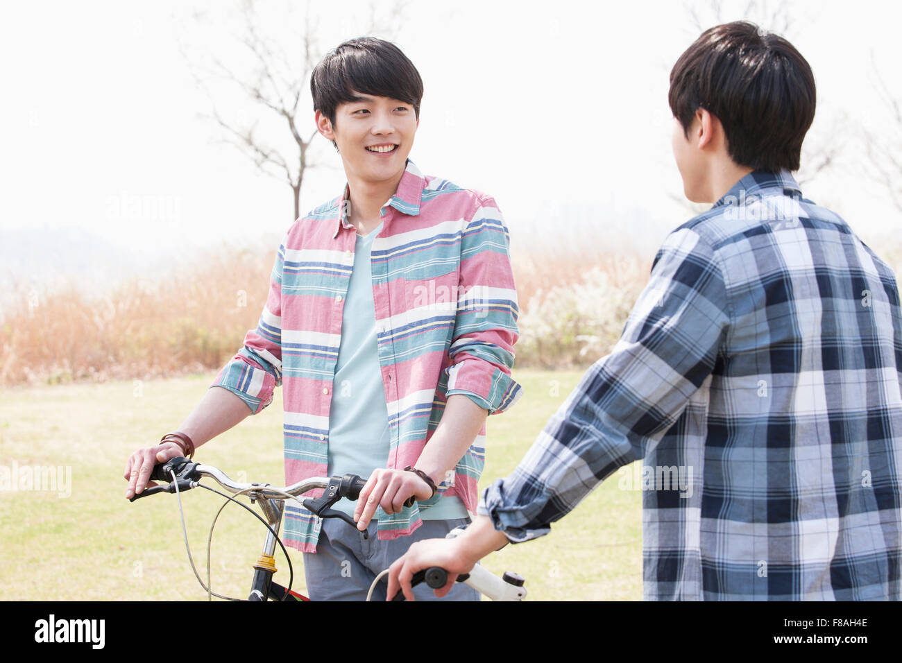 Two men with their bikes looking at each other and smiling in the park Stock Photo