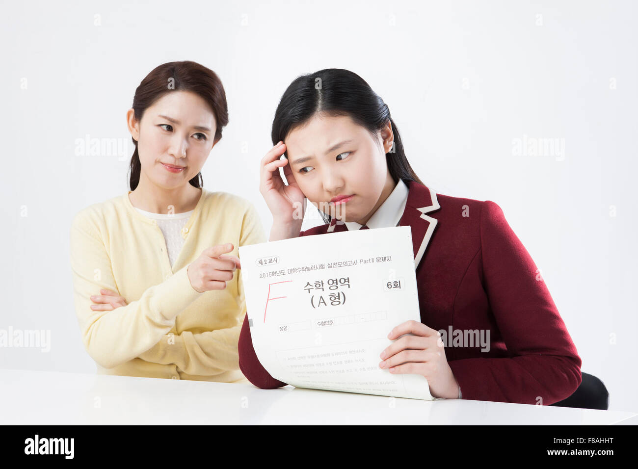 Mother scolding her daughter with pointed finger and daughter with a test result of F Stock Photo