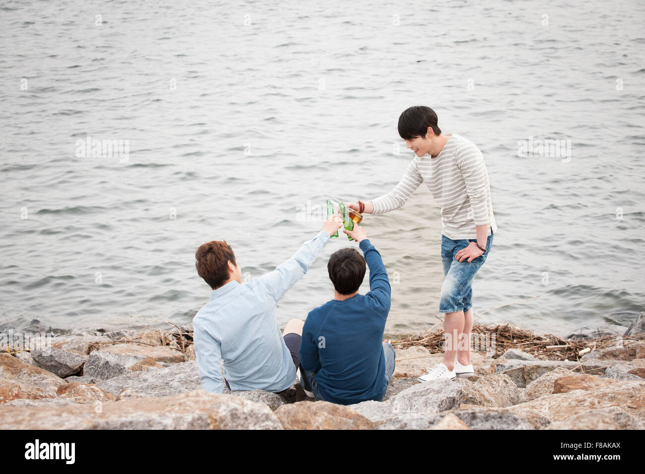 Three young men toasting with beers at the riverside Stock Photo