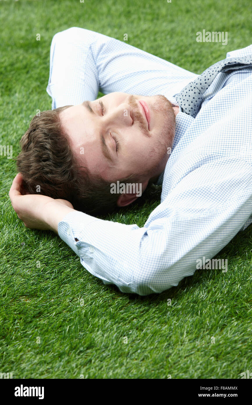 Portrait of businessman lying down pillowing his head on his hands with closed eyes on grassland Stock Photo