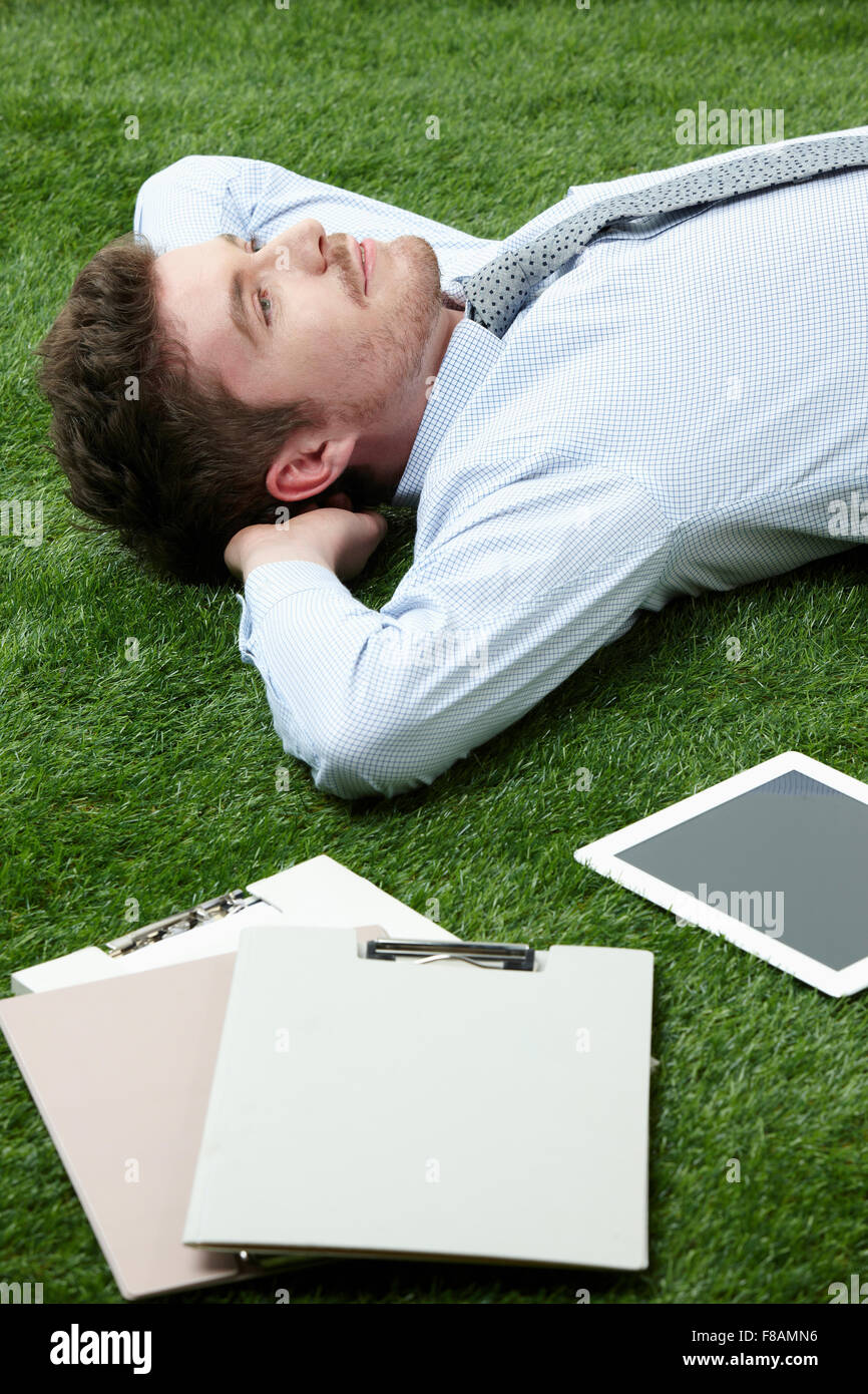 Portrait of businessman lying down on grassland looking up Stock Photo