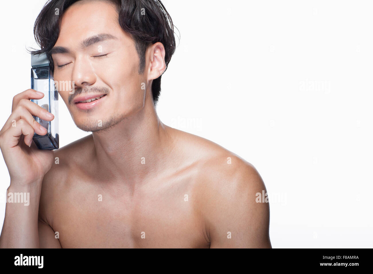 Portrait of young Asian man pressing his face against a cosmetic in his hand with closed eyes Stock Photo