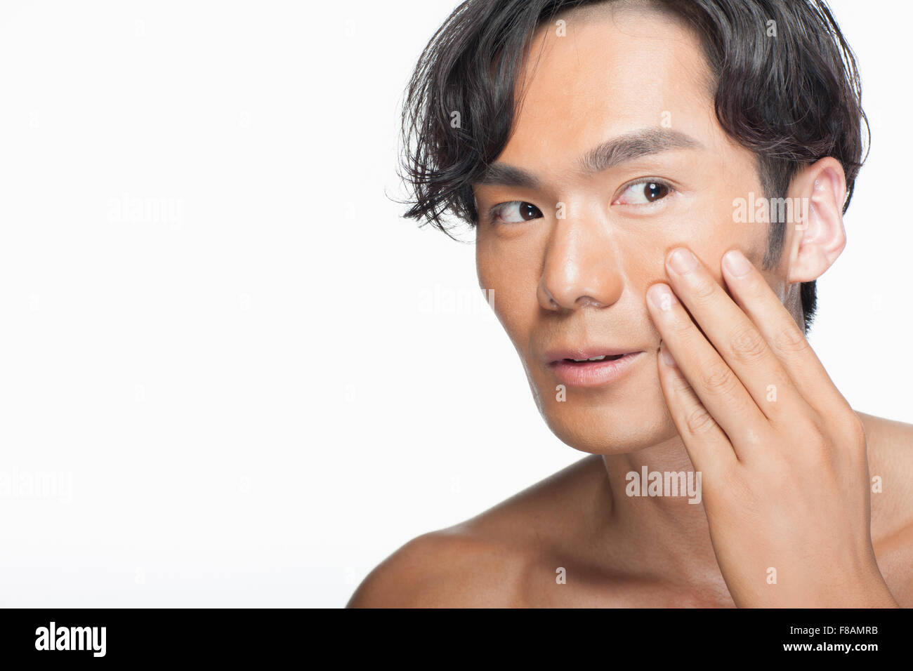 Portrait of young Asian man touching his cheek looking up Stock Photo