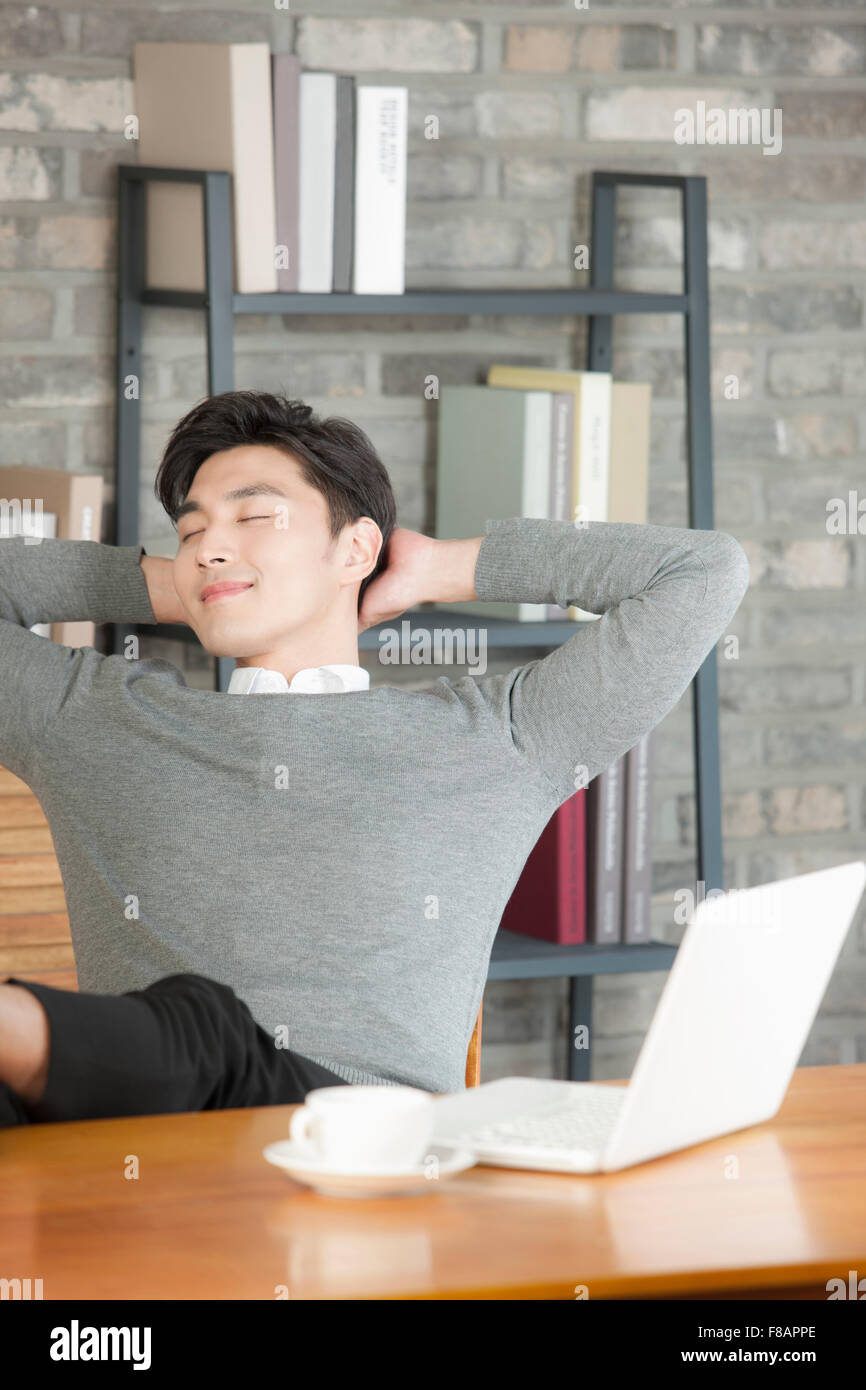 Side view portait of young smiling businessman relaxing with closed eyes and hands under head at cafe Stock Photo