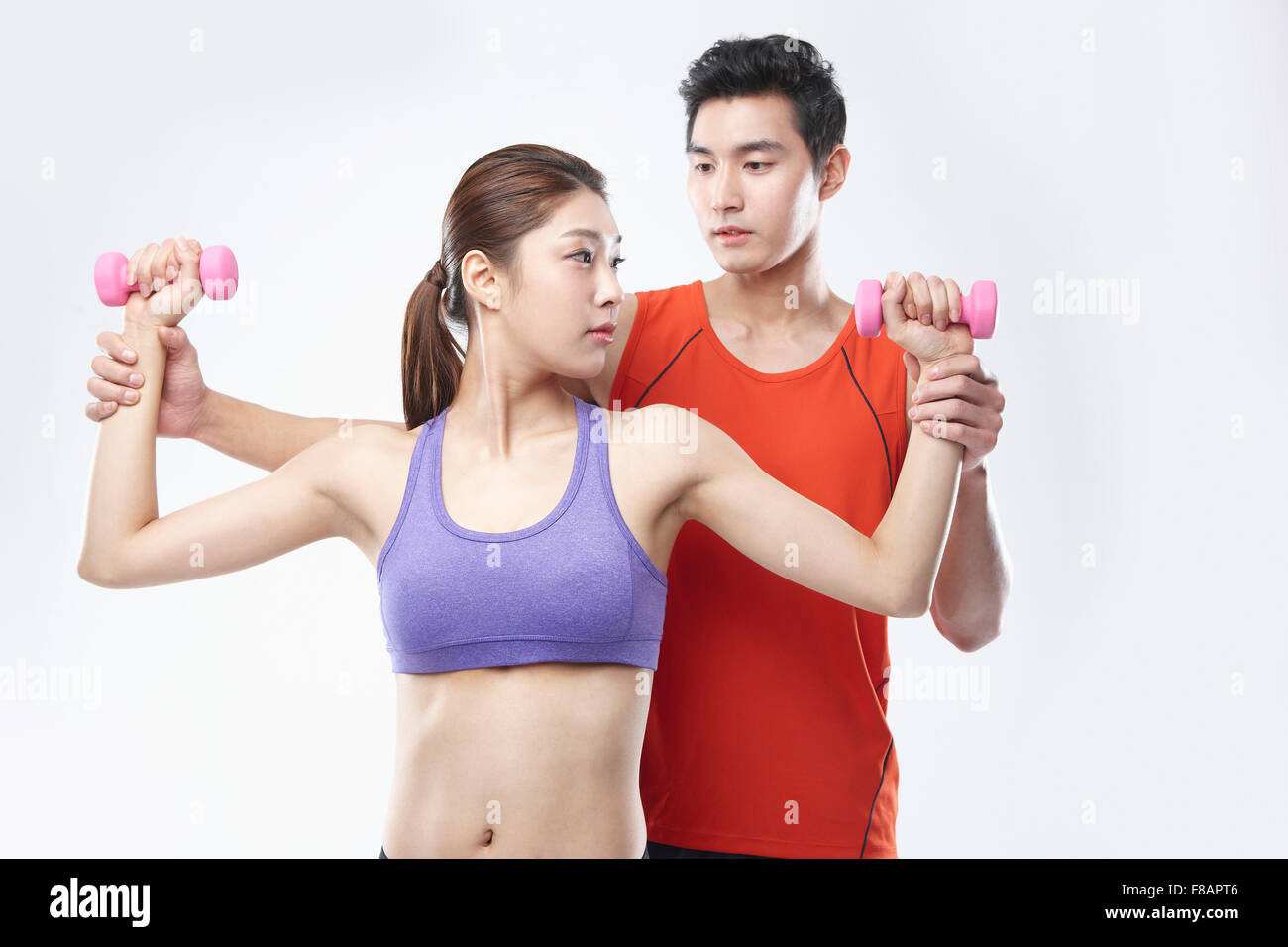 Portrait of woman lifting dumbbells and opening arms with a male health trainer helping her Stock Photo
