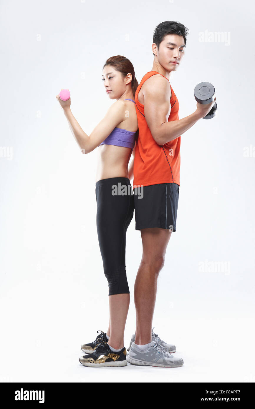 Couple standing back to back holding dumbbells looking down Stock Photo