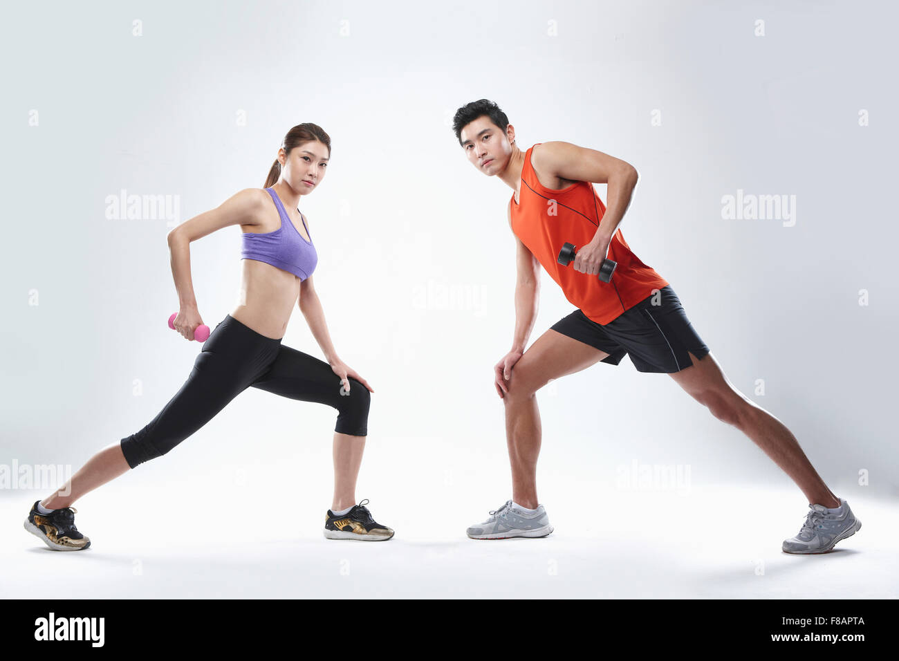 Couple lifting dumbbells spreading feet, standing face to face staring at front Stock Photo