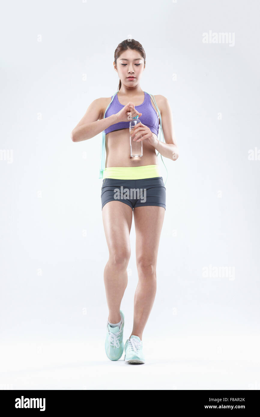 Confident woman in sportswear standing with jump rope and uncapping water bottle looking down Stock Photo