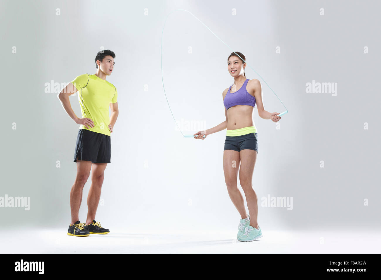 Man in sportswear standing with hands on waists, woman in sportswear jumping rope with a smile Stock Photo