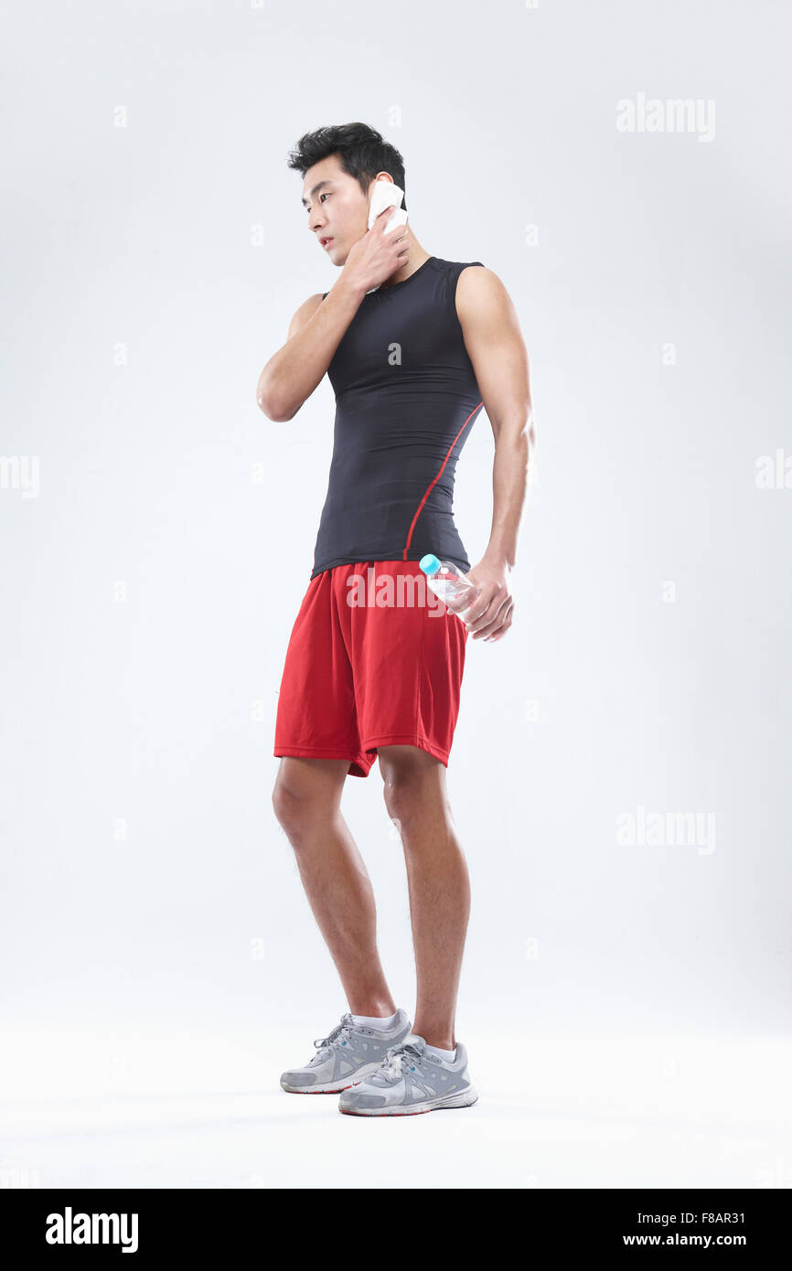 Man in sportswear wiping the sweat holding a water bottle looking down Stock Photo