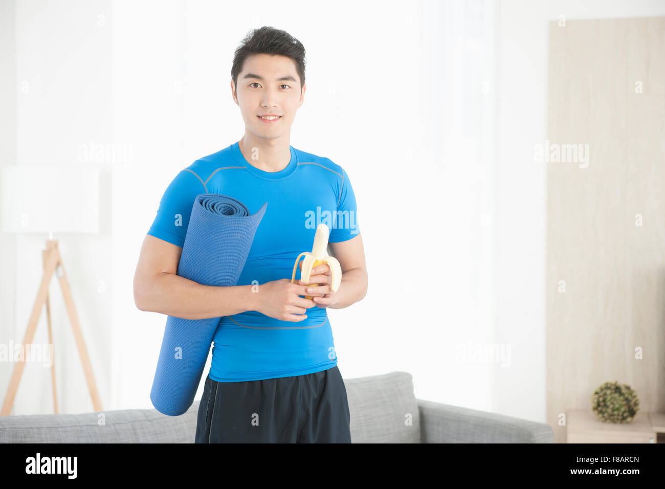 Man holding a mat and banana staring at front in living room Stock Photo