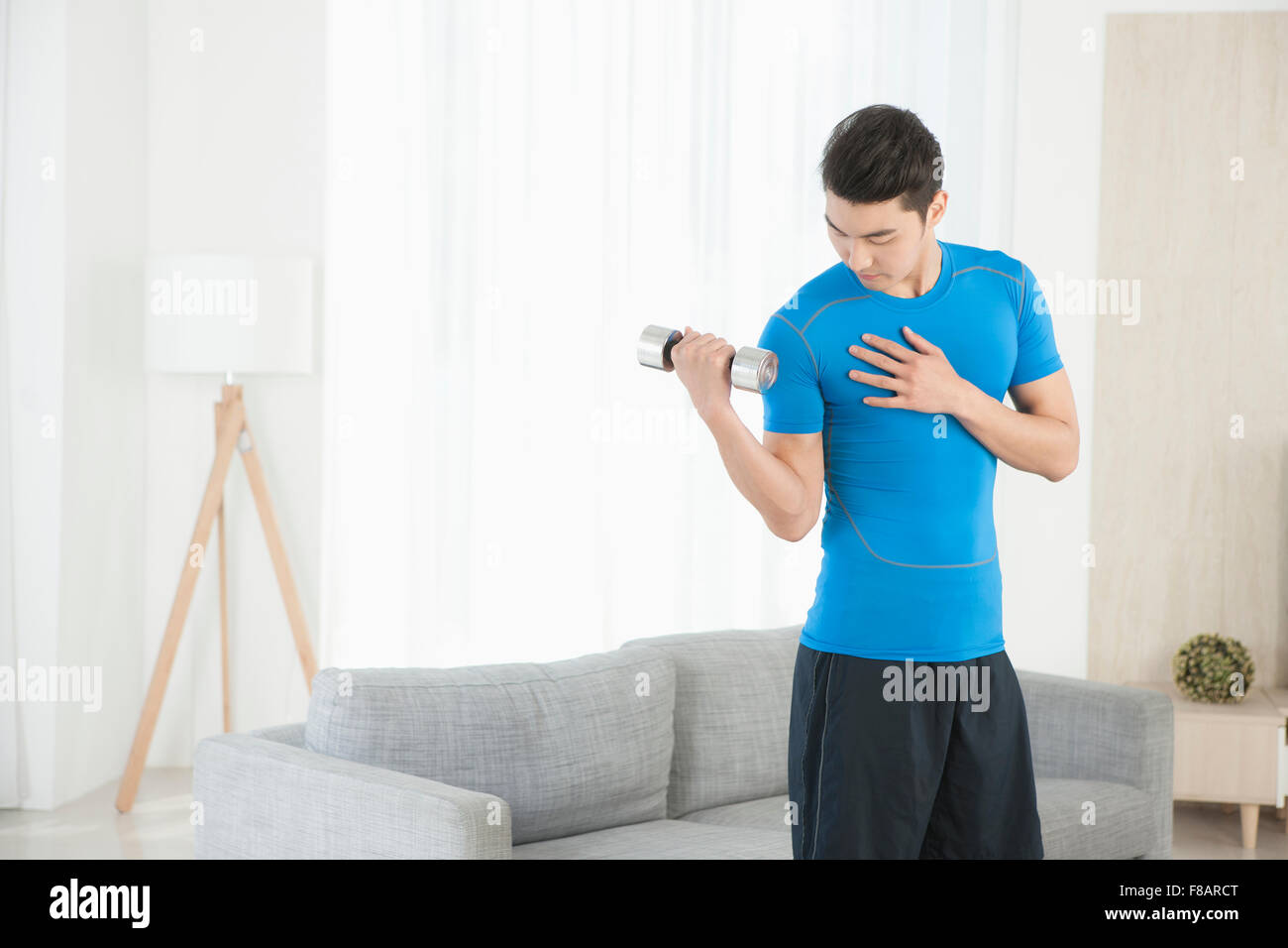 Man holding a dunbbell looking down in living room Stock Photo