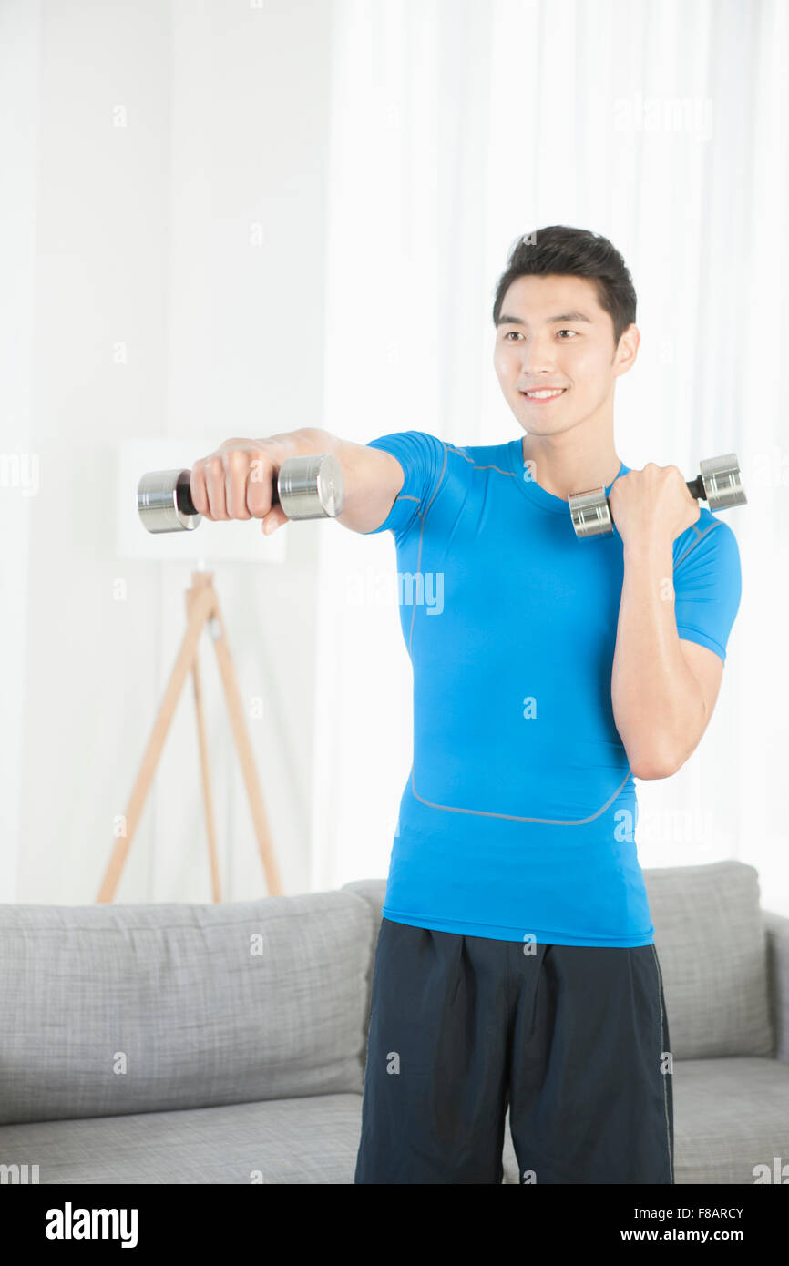Man standing and exercising with dumbbells in living room with a smile Stock Photo