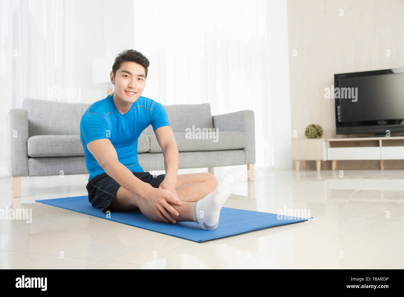 Man sitting and stretching on mat staring at front in living room Stock Photo