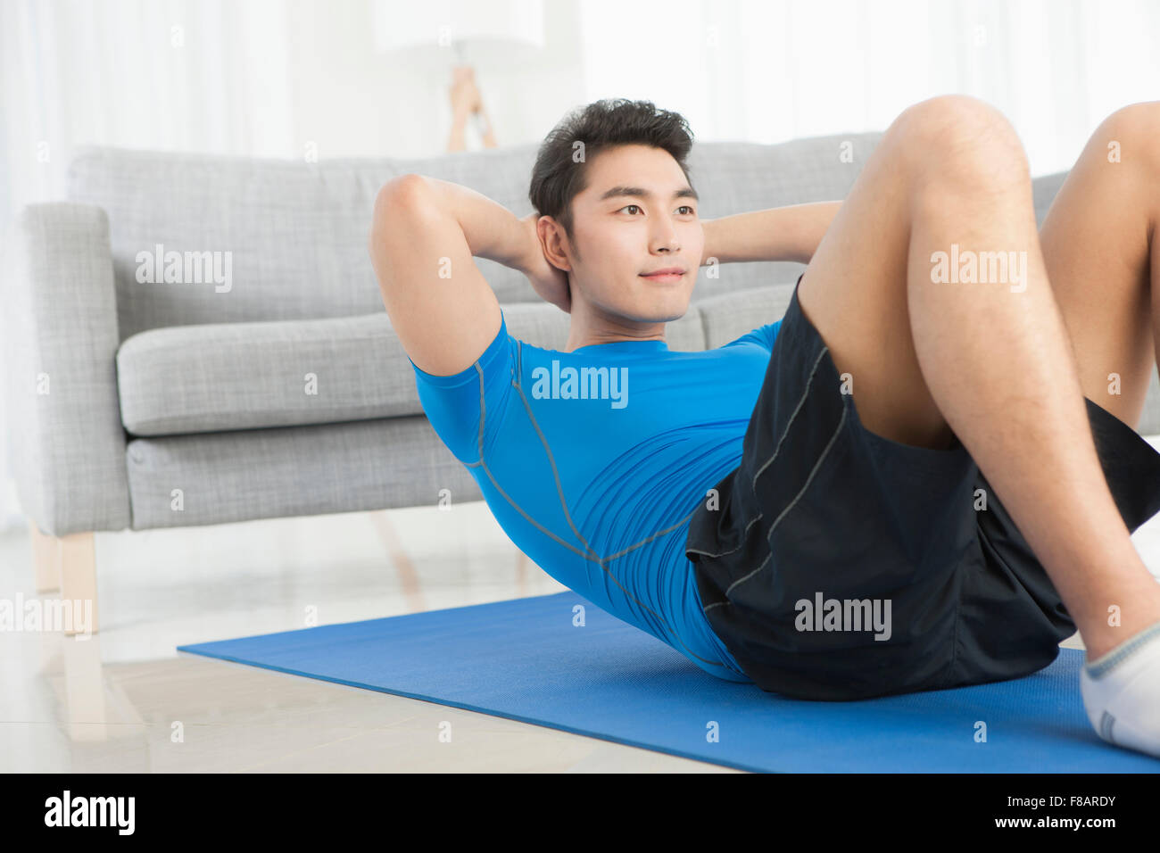 Man doing sit-up on mat in living room Stock Photo