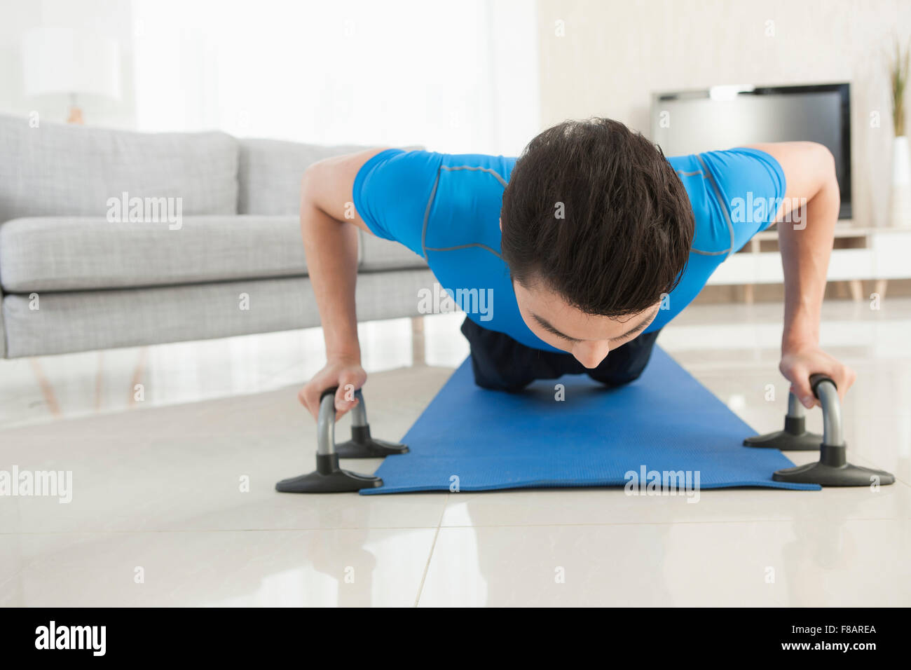 Man lying face down and doing pushups on mat in living room looking