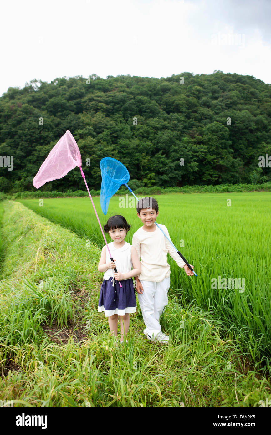 Smiling boy and girl standing with nets staring at front on lane through rice fields in spring