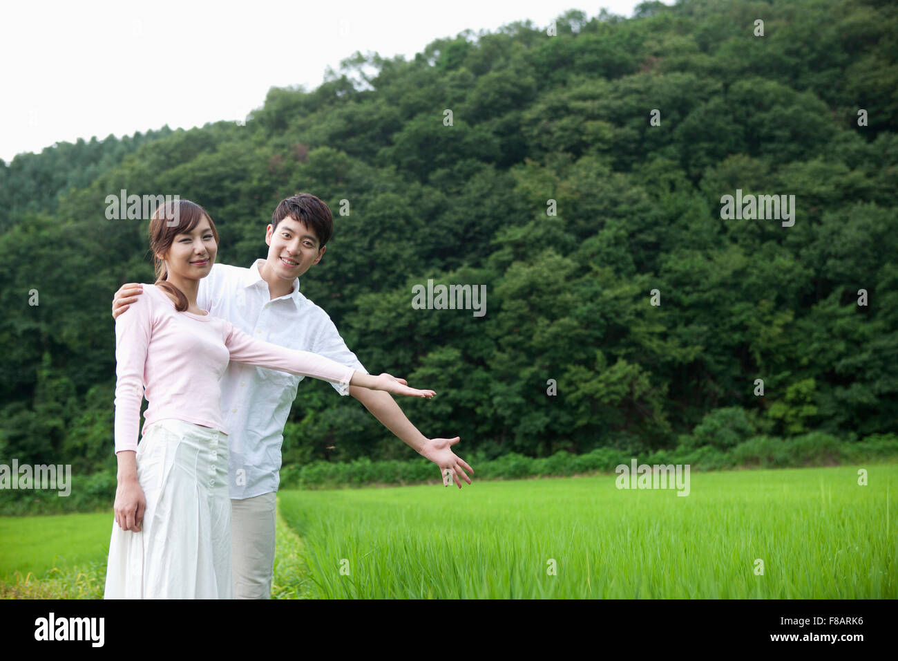 Smiling couple holding out hands placing hand on shoulder agains rice fields and mountain in spring Stock Photo