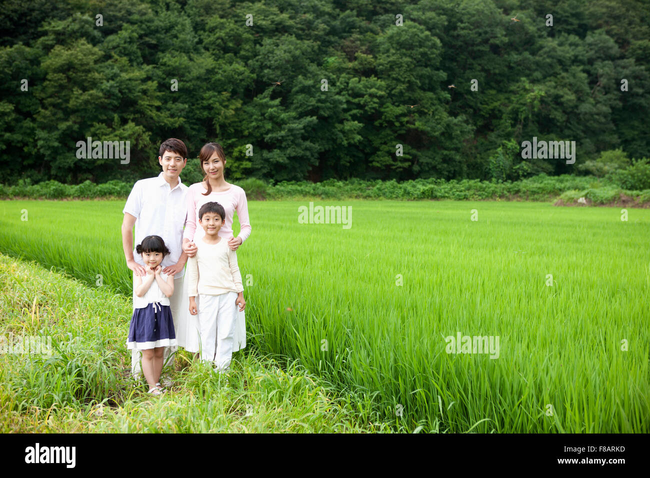 Sweet family standing with smiles on lane against rice fields and mountain Stock Photo