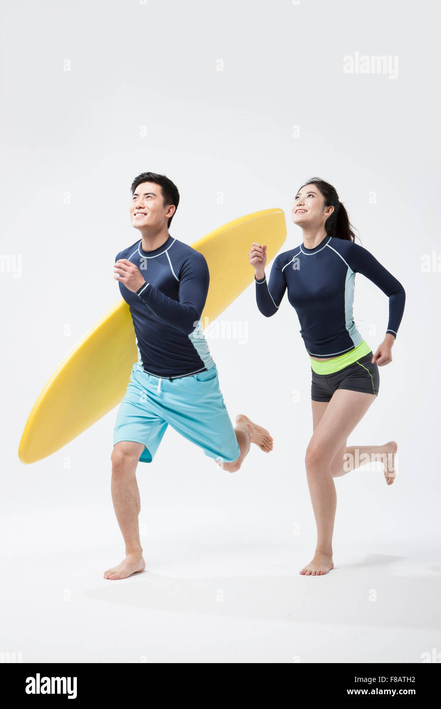 Couple running with a surfing board looking up with smiles Stock Photo