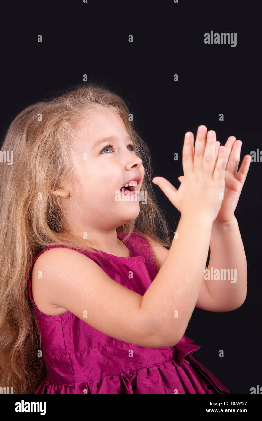 Little cute girl in a pink dress on a black background in the studio ...