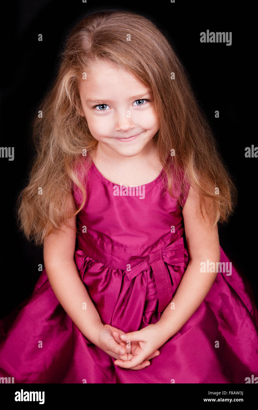 Portrait of a cute little girl in a pink dress on a black background ...
