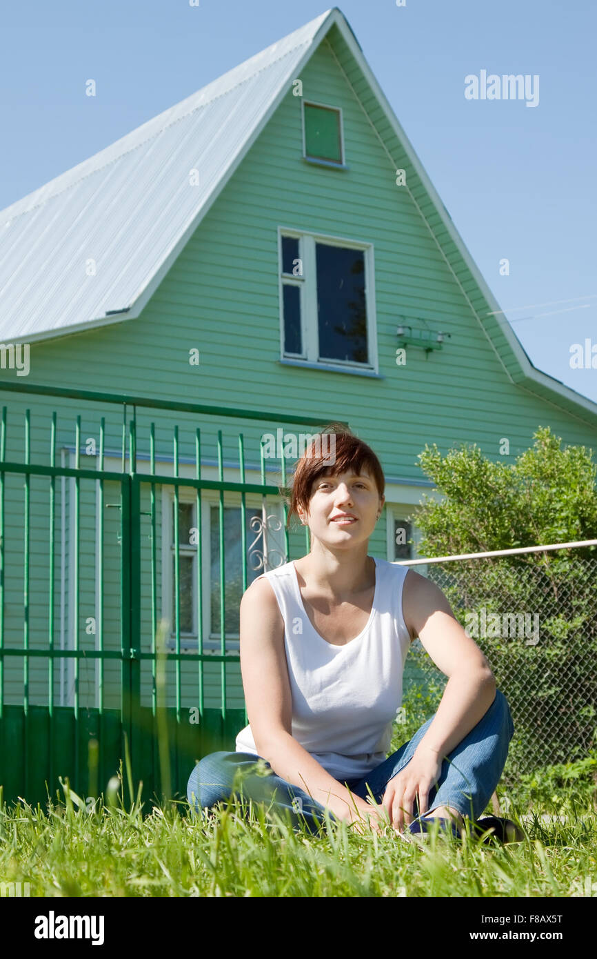 Happy young woman sitting on lawn in front of new home Stock Photo - Alamy