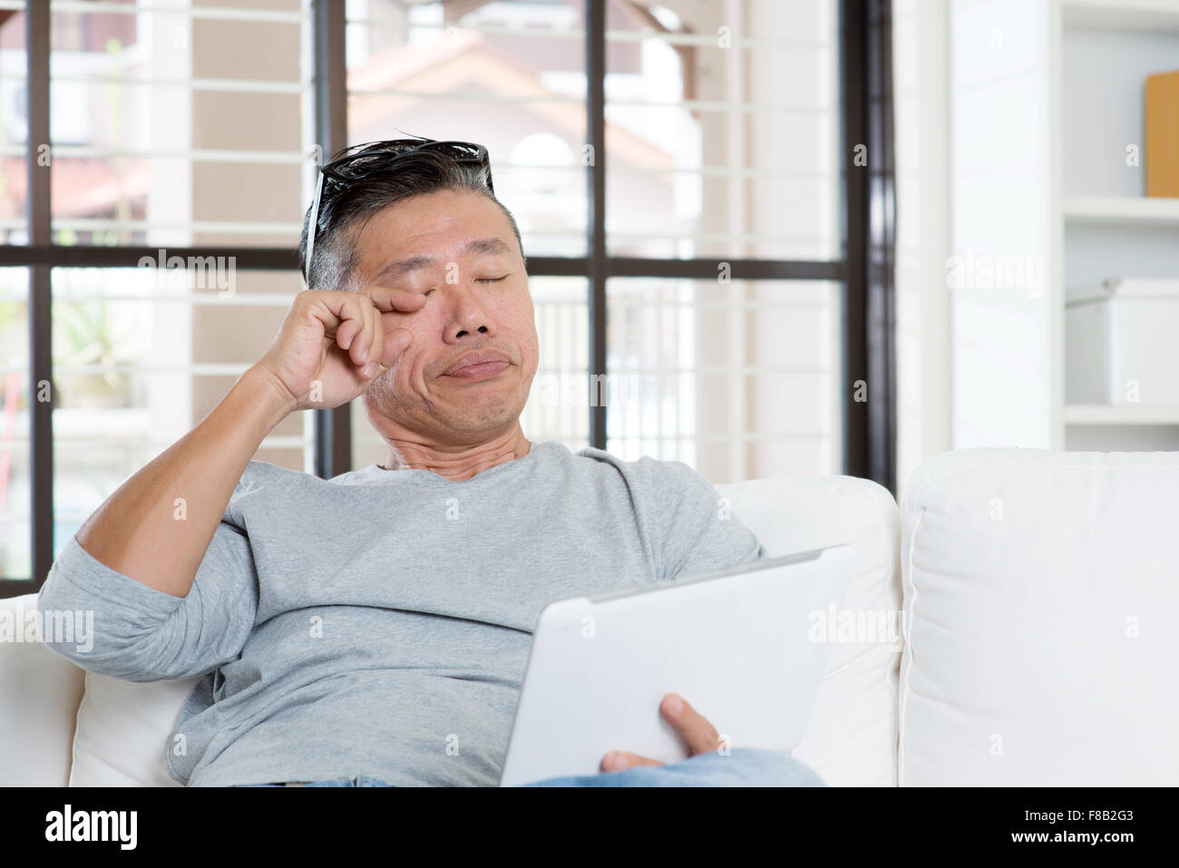 Portrait of 50s mature Asian man eyes pain, rubbing eye with tired expression after long period using tablet computer, sitting o Stock Photo