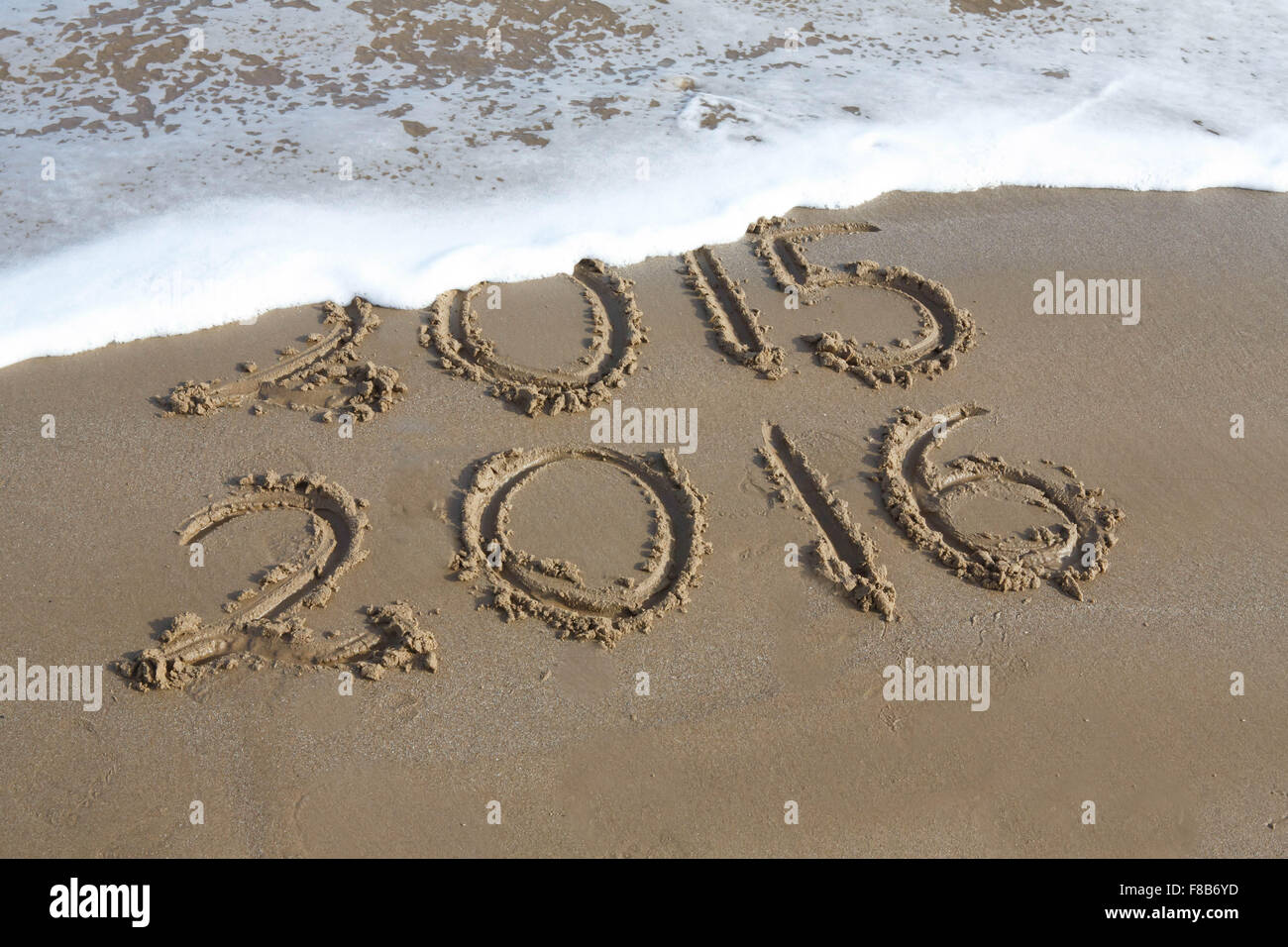 The new year is coming, with the date 2015 and 2016 written on a beach , with the year 2015 starting to be erased by a wave. Stock Photo