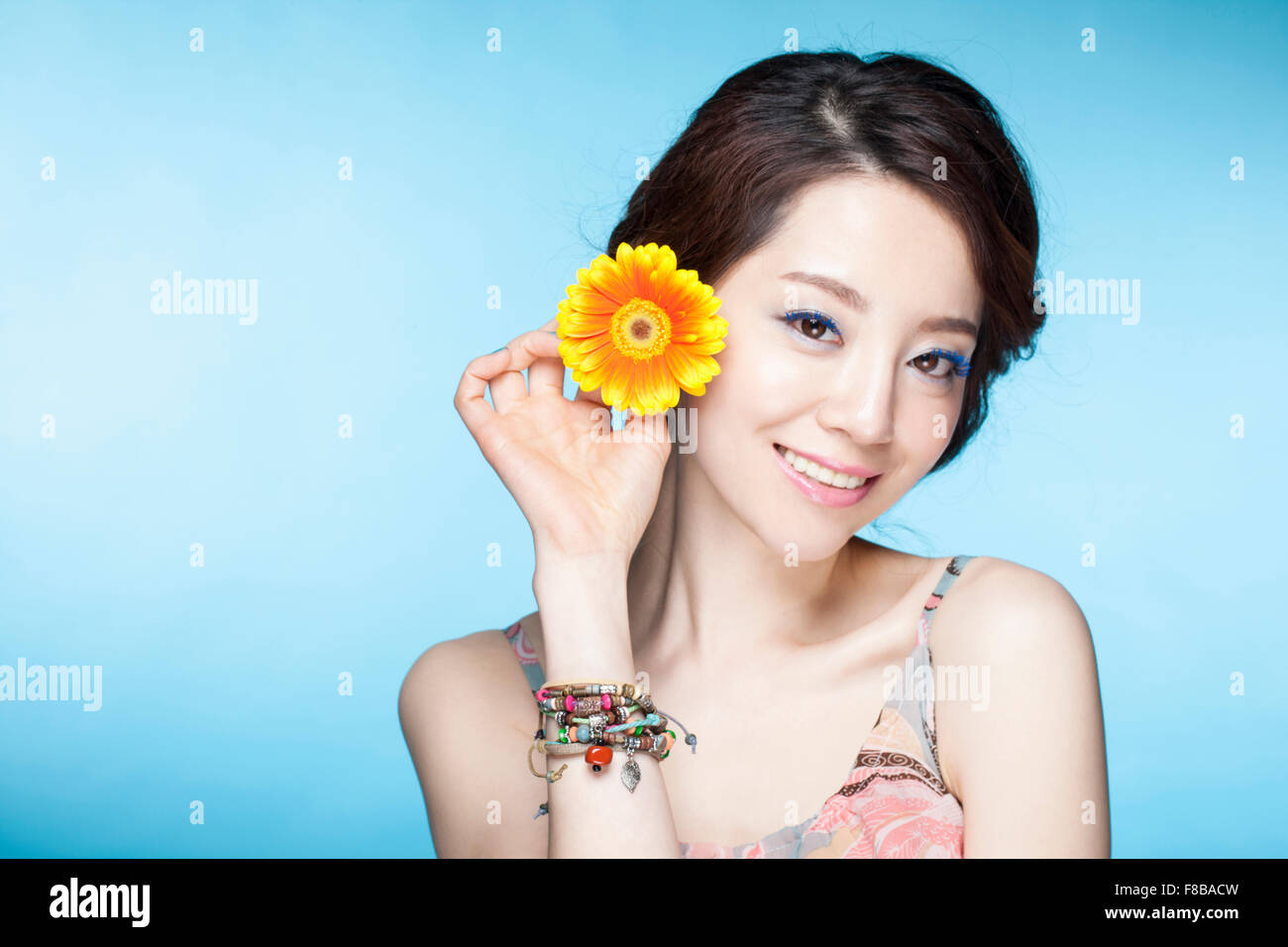 Woman in summer wear smiling and holding a flower close to her ear Stock Photo
