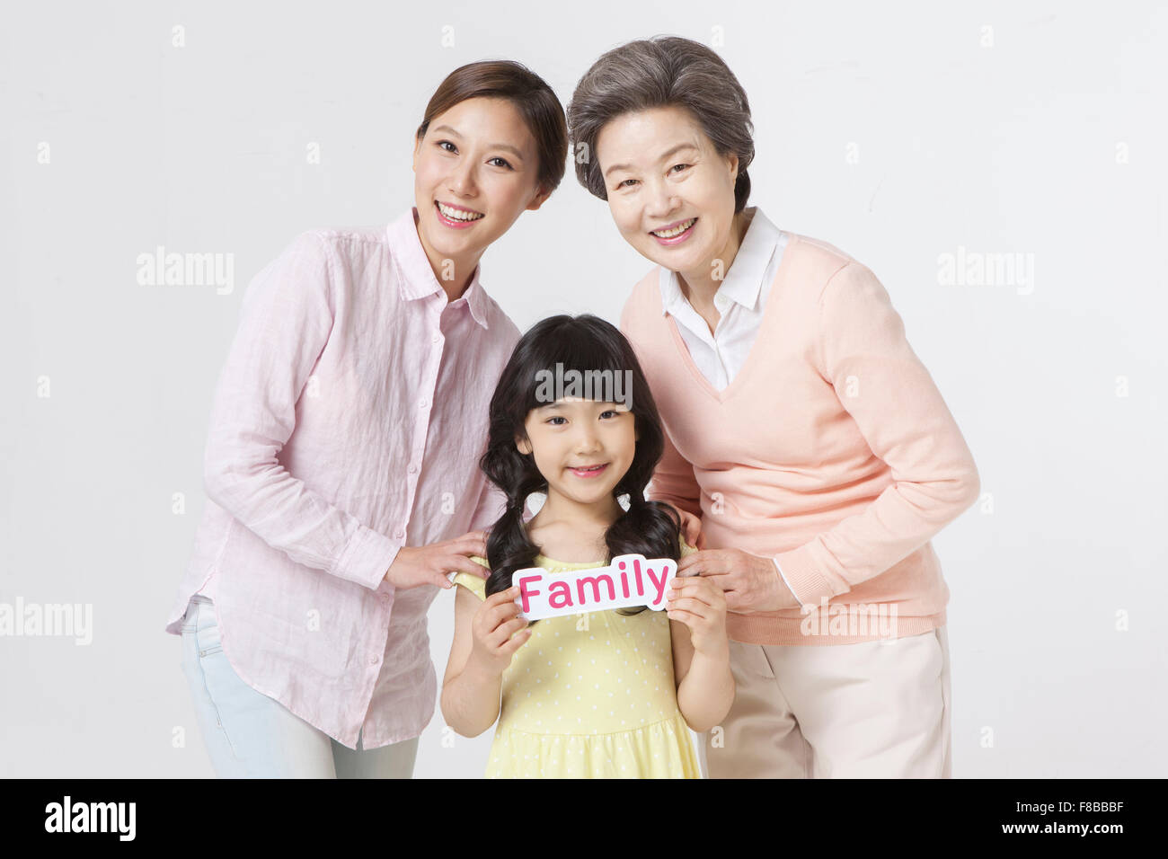 Mother, grown-up daughter, and granddaughter standing close to each other and granddaughter holding word Family Stock Photo