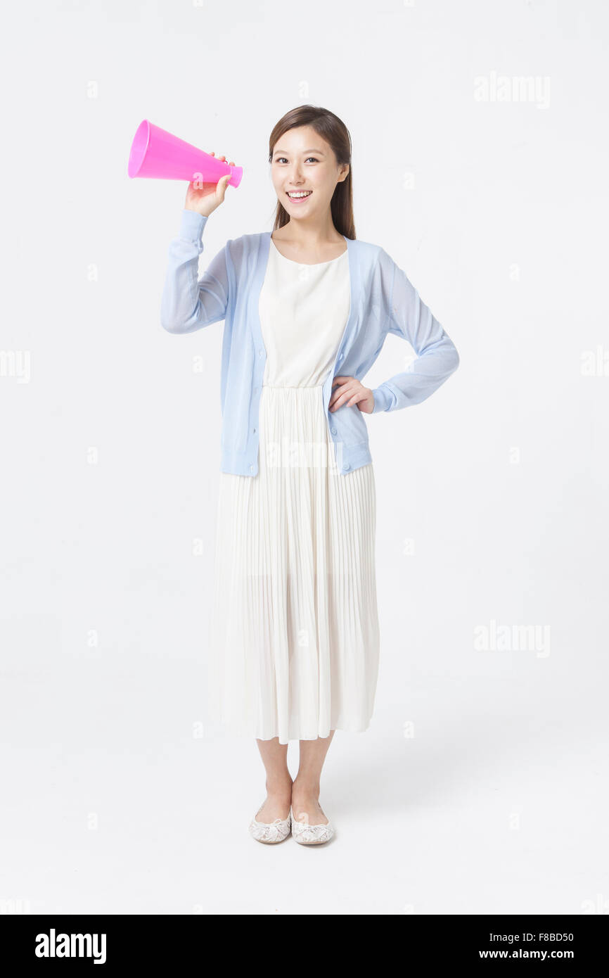 Woman in white dress and blue cardigan holding a fake megaphone with her hand on her waist and staring forward with a smile Stock Photo