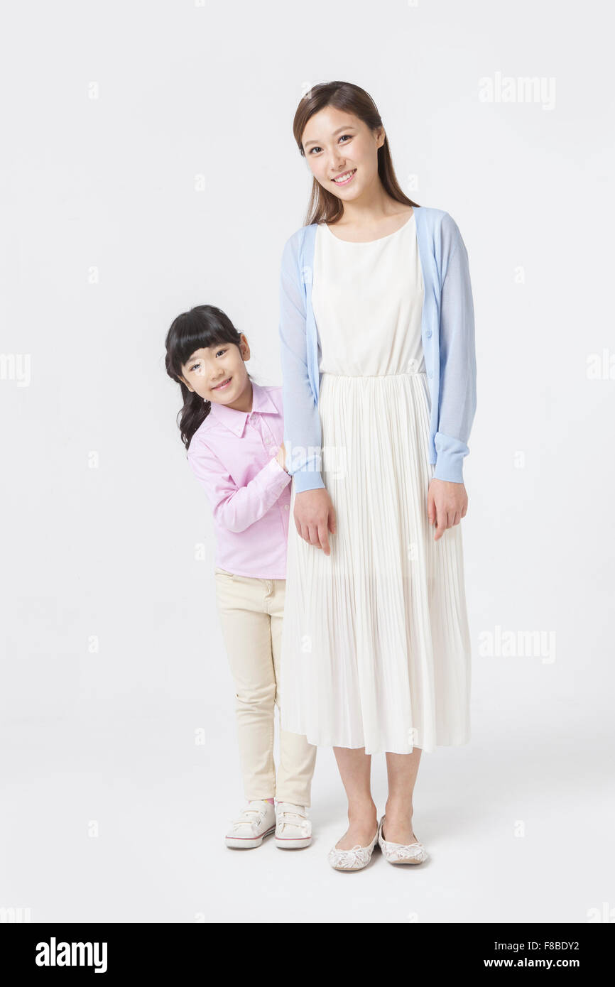 Daughter standing behind her mother both staring forward and smiling