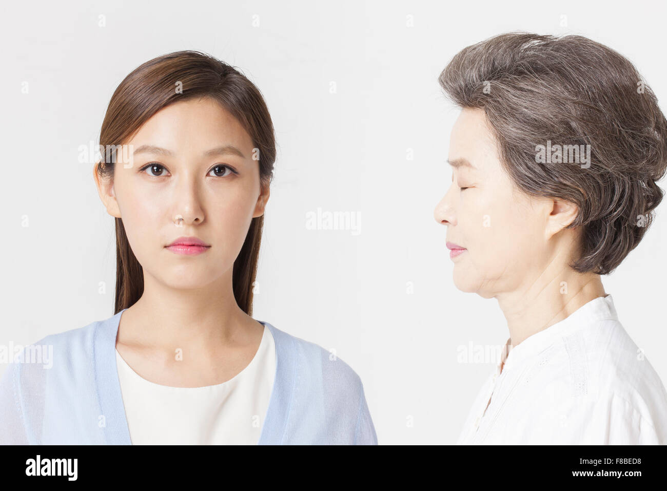 Daughter staring forward with no facial expression and mother facing her daughter with her eyes closed Stock Photo