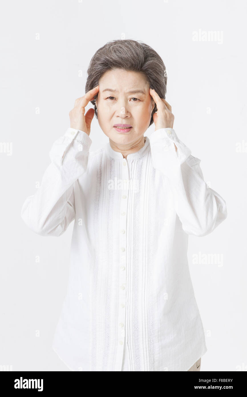 Grandmother with short hair in white shirt touching her head with frowned face and staring forward Stock Photo