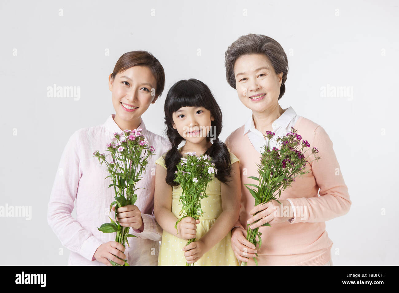 Young adult woman, young girl, and senior woman all holding flowers and staring forward with a smile Stock Photo