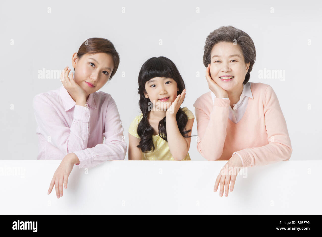 Young adult woman, young girl, and senior woman resting their arms on a white copy space with their head resting in the other Stock Photo