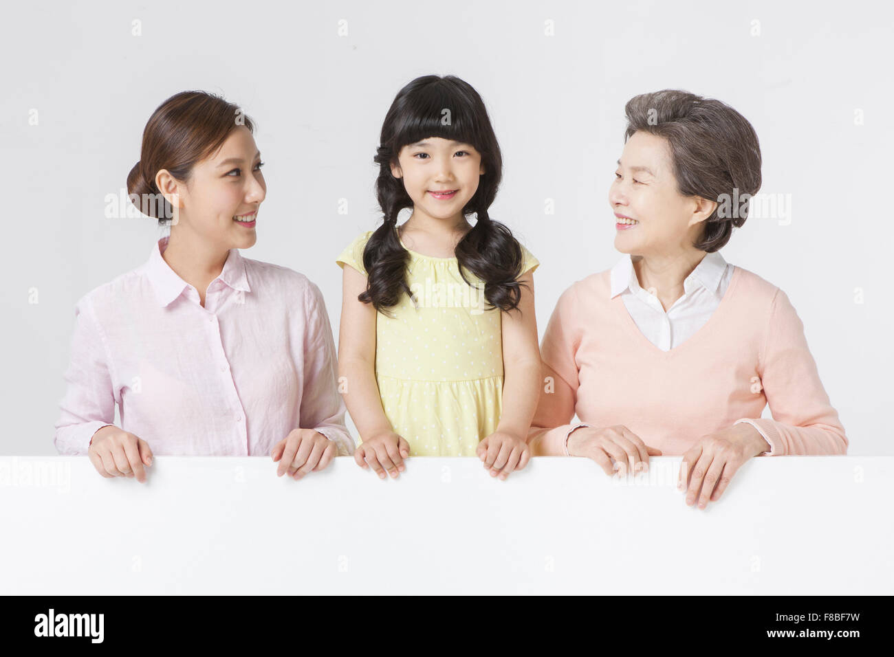Young adult woman and senior woman looking at the young girl between them and all placing their hands on the white copy space Stock Photo