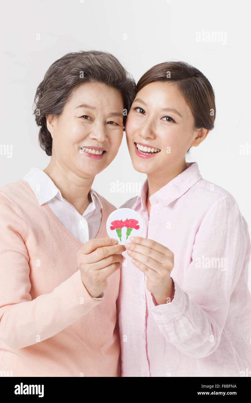 Mother and daughter holding an emblem of carnation flowers and staring forward with a smile Stock Photo