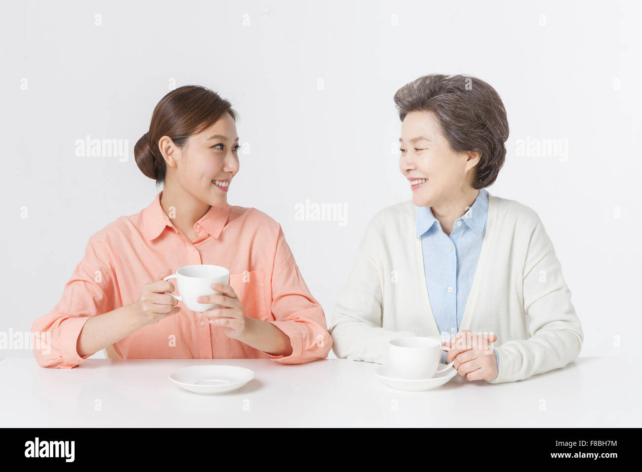 Mother and daughter seated at table having tea time and looking at each other with a smile Stock Photo