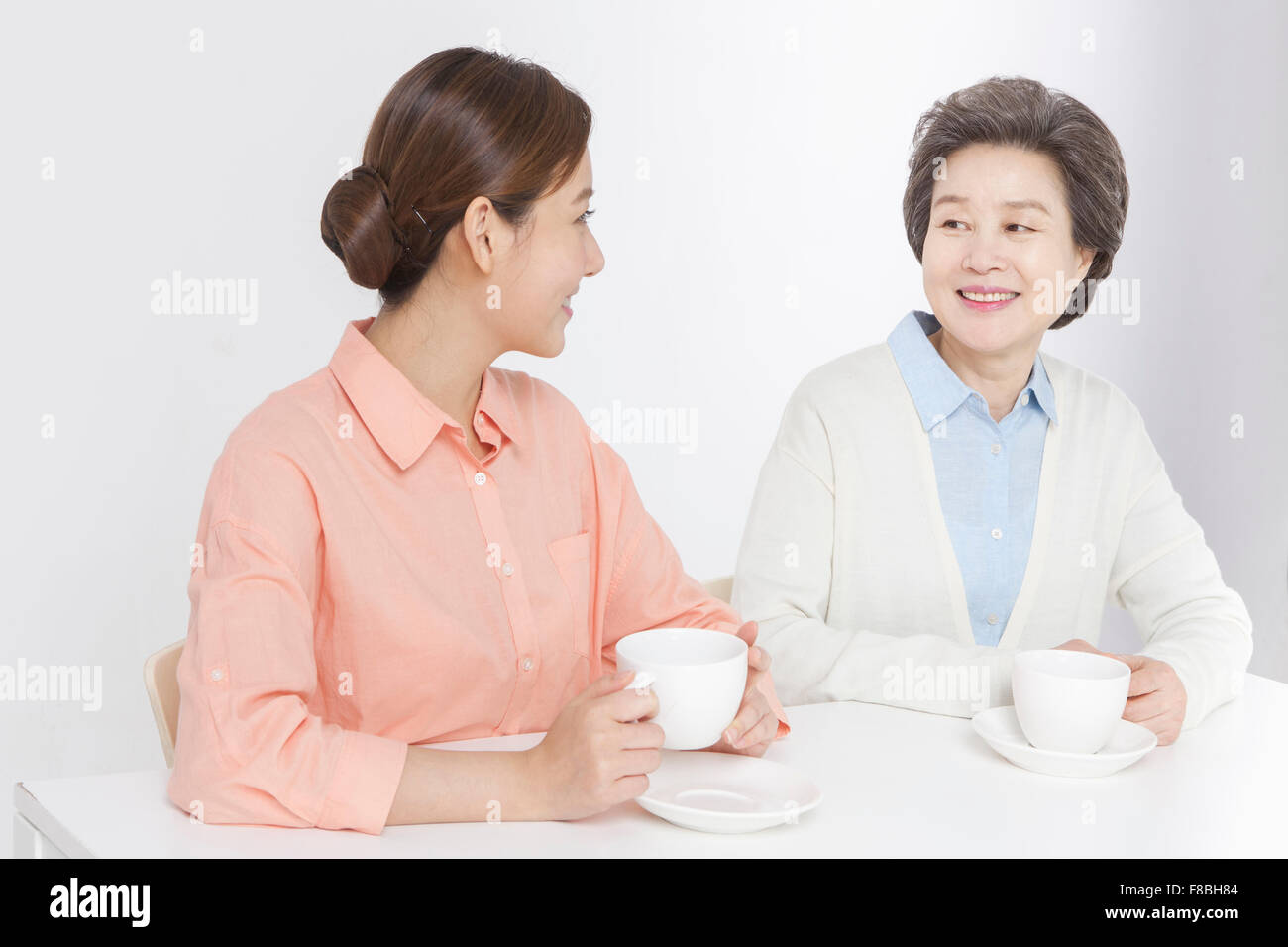 Mother and daughter seated at table having tea time and looking at each other with a smile Stock Photo